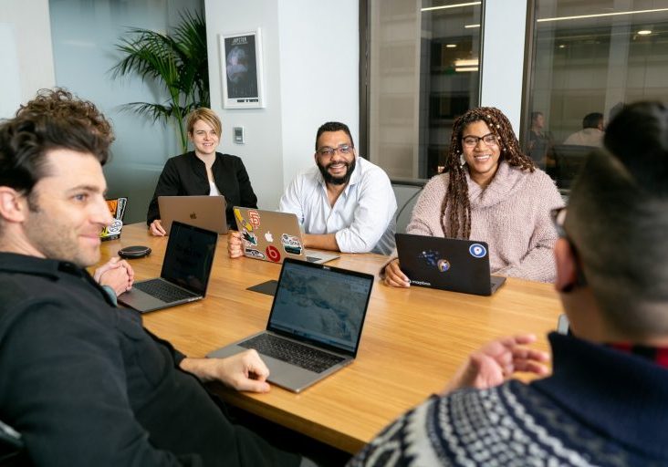 A group of people sitting around a table with laptops.